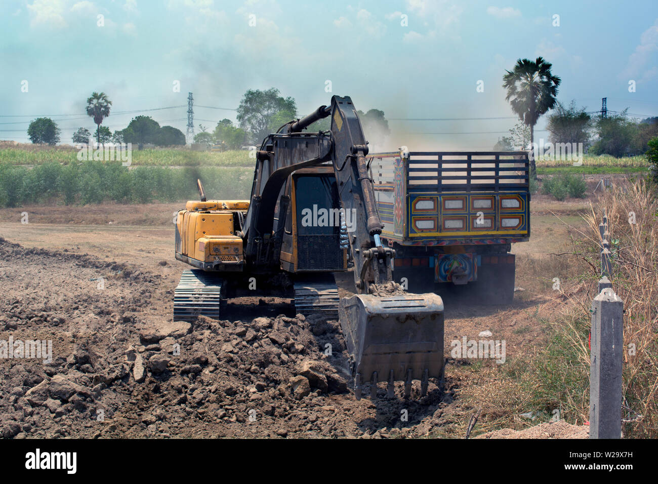 Backhoe digging to fill soil in dump truck at construction site Stock