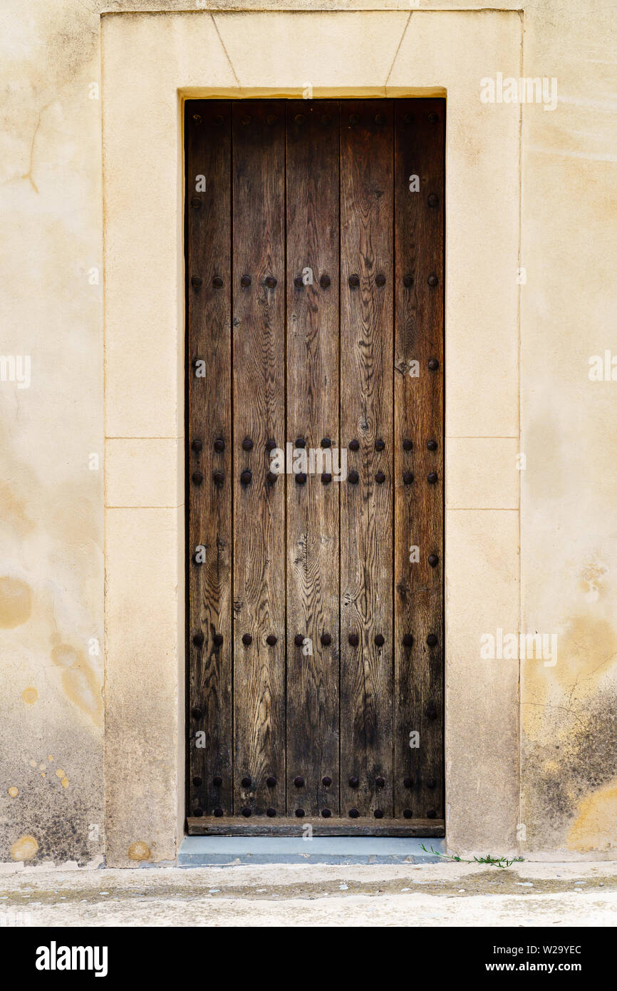 Massive wooden door with rivets and beautiful natural grain in a weathered stone wall, door closed - vertical portrait orientation Stock Photo