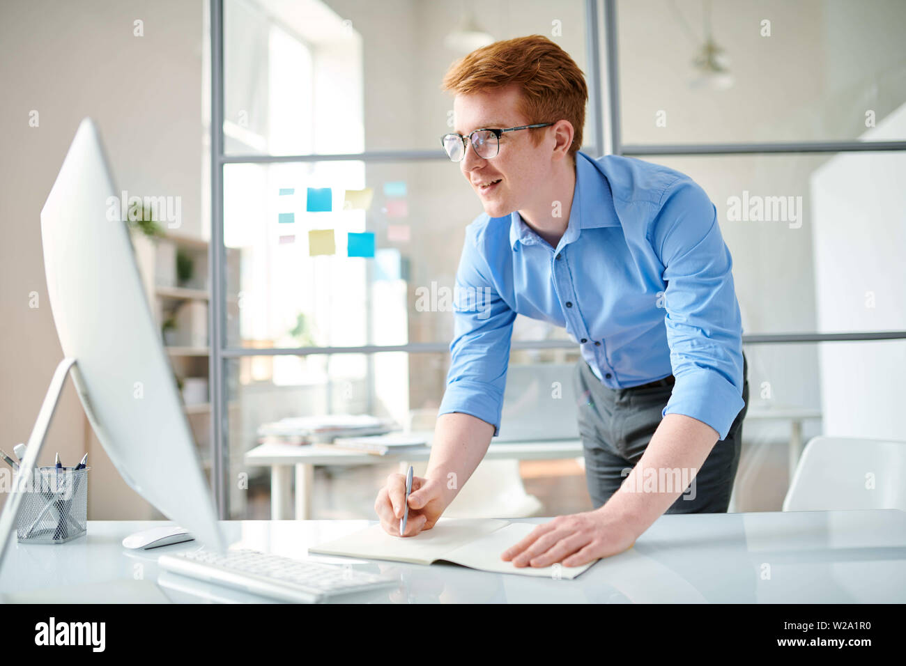 Young programmer making notes while watching video for webdesigners Stock Photo