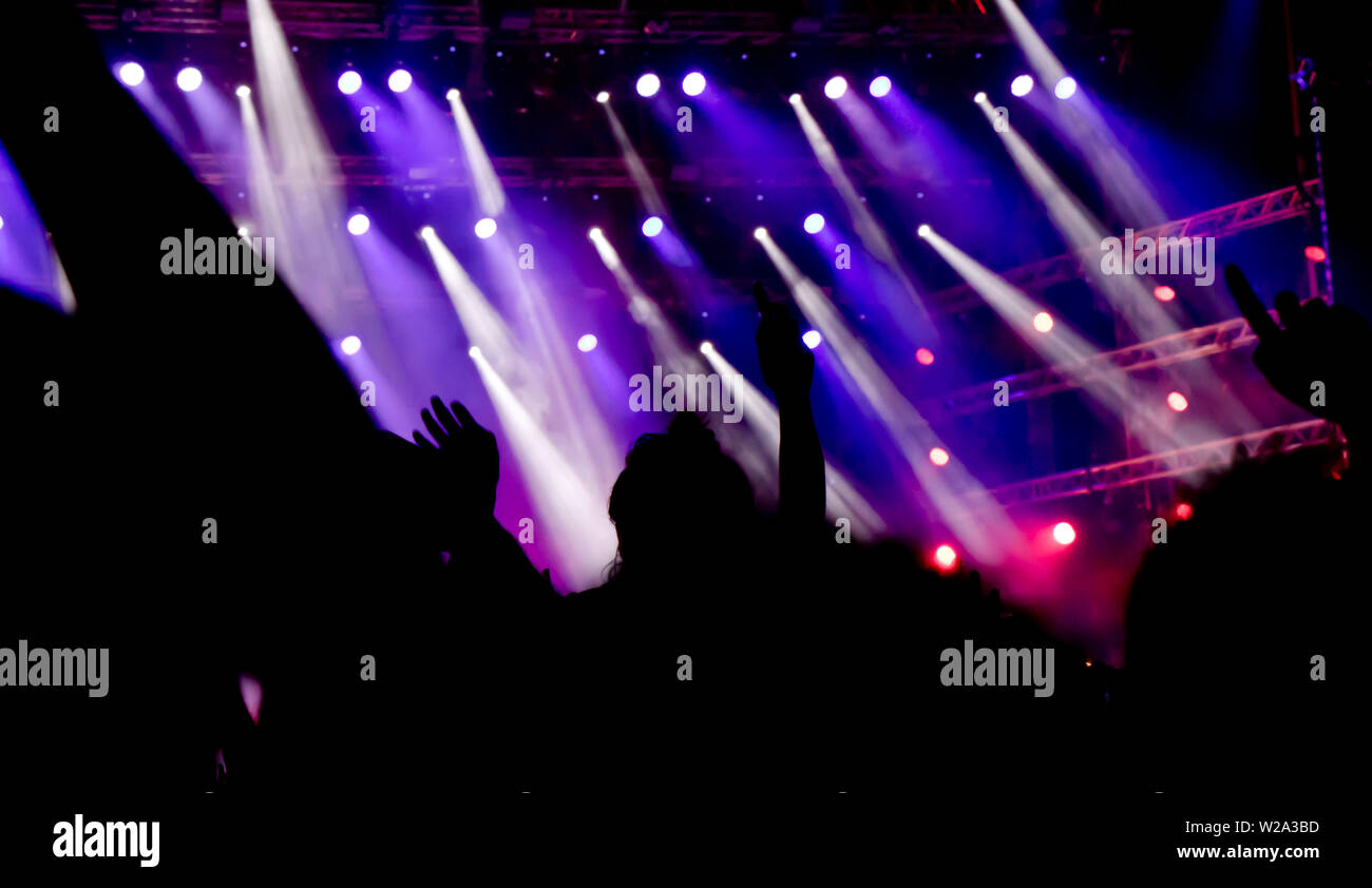 Blurry silhouettes of people with raised hands on the concert, from behind Stock Photo