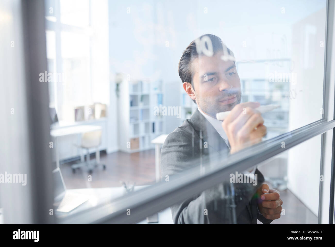 Young coach writing down working notes on transparent board Stock Photo