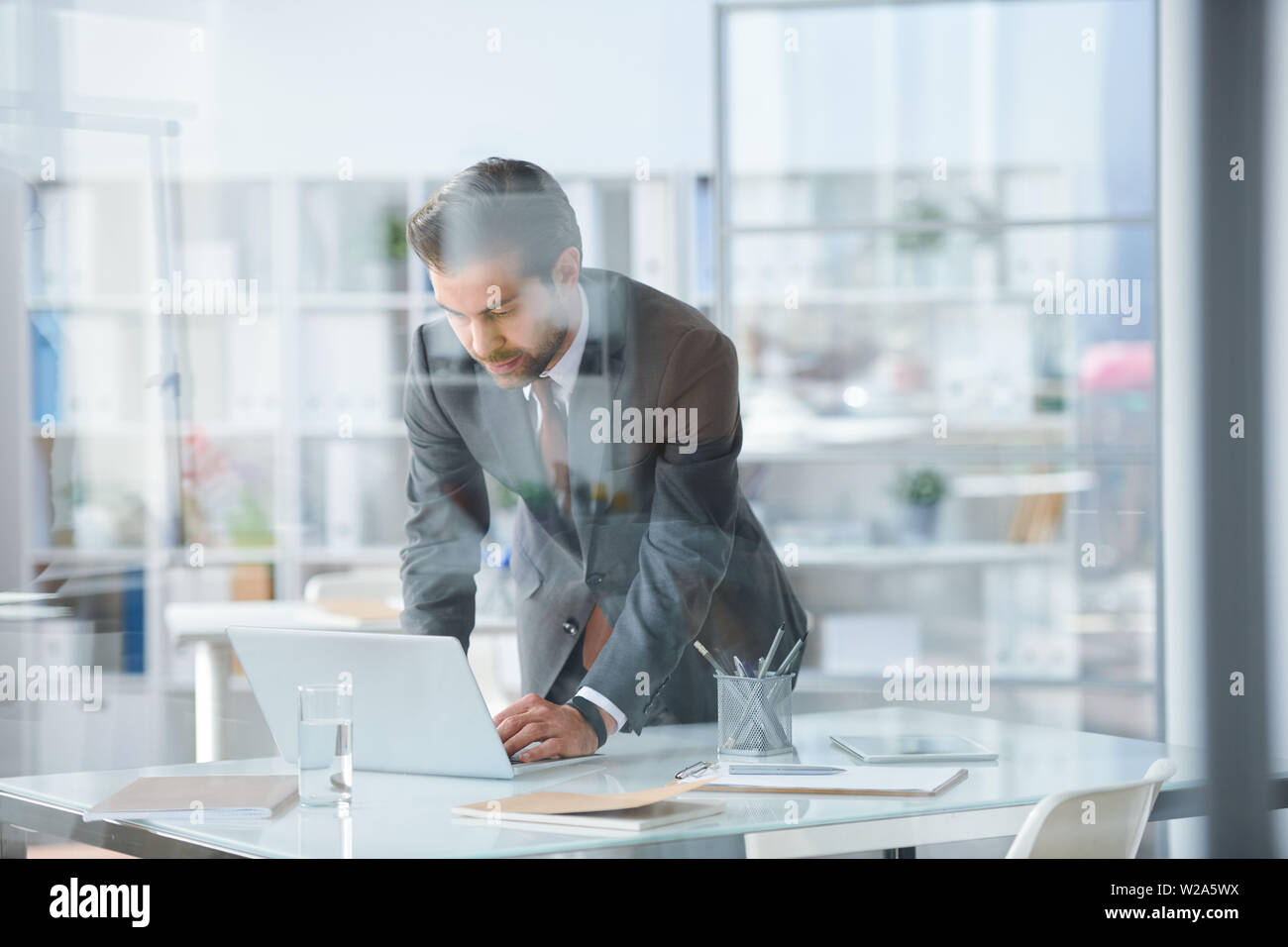 Young elegant businessman bending over desk and laptop Stock Photo - Alamy