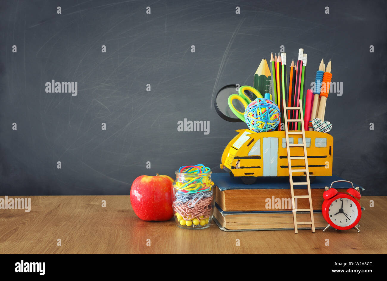 education and back to school concept. pencils stand as bus over wooden desk infront of classroom blackboard Stock Photo
