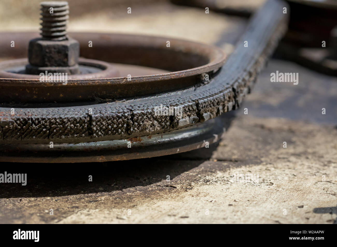 Old, cracked, and worn drive belt and pulley on a lawn mower deck needing maintenance Stock Photo