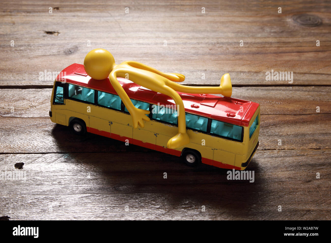 Figure Lying on Top of Toy Bus with Wooden Background Stock Photo