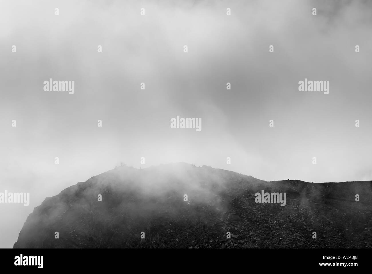 Misty, dramatic, black and white view of Lakes peak on Rila mountain, famous vantage point of seven Rila lakes, with silhouette hikers at the top Stock Photo