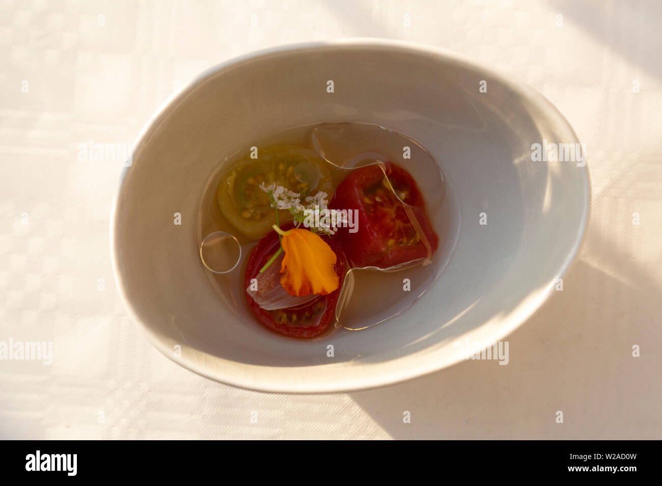 Tomatoes served in an oil with a chilli infusion and edible flowers. Stock Photo