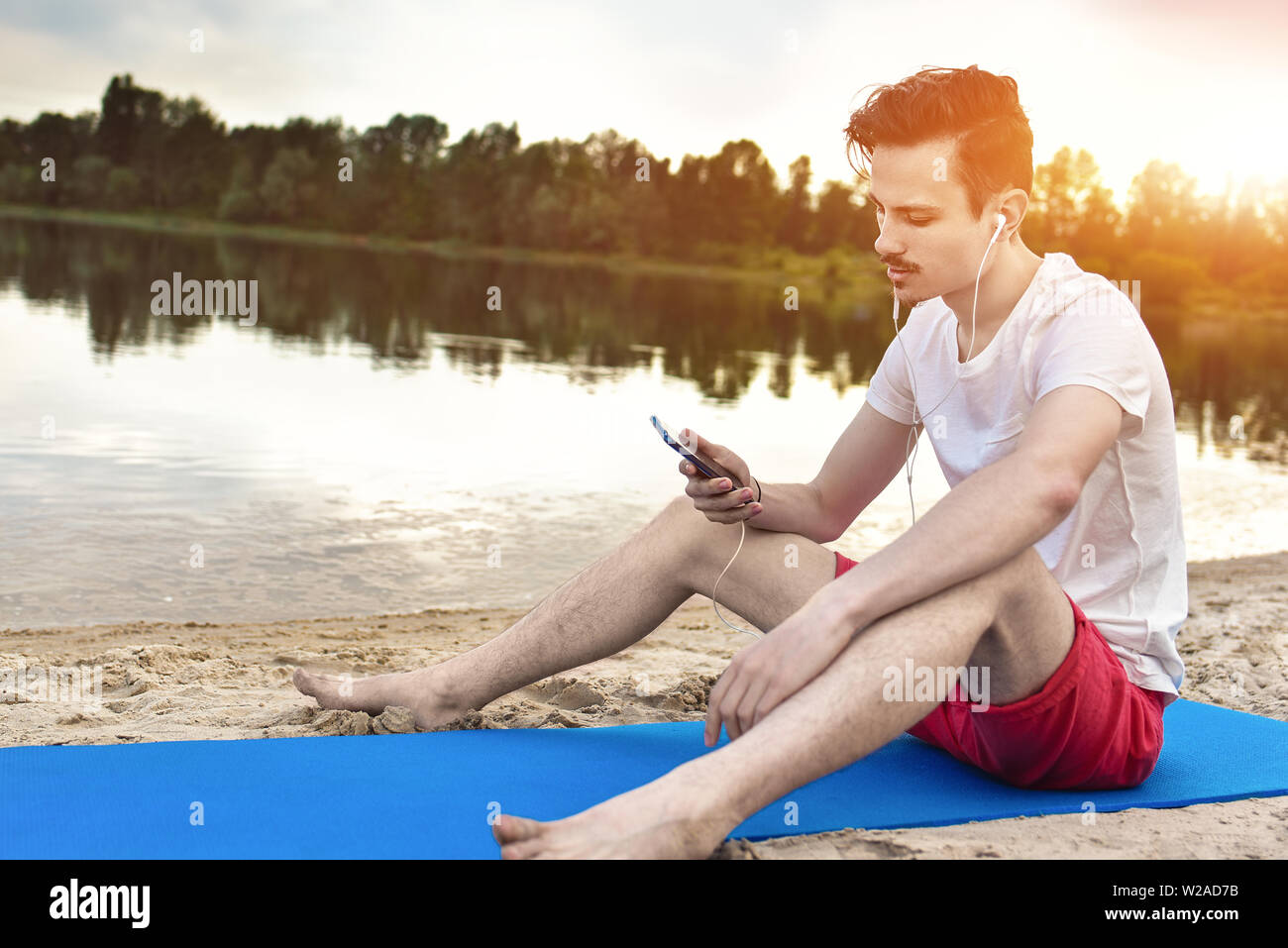 Man is sitting on the beach at lake and writing a sms on phone. good mood. beautiful view Stock Photo