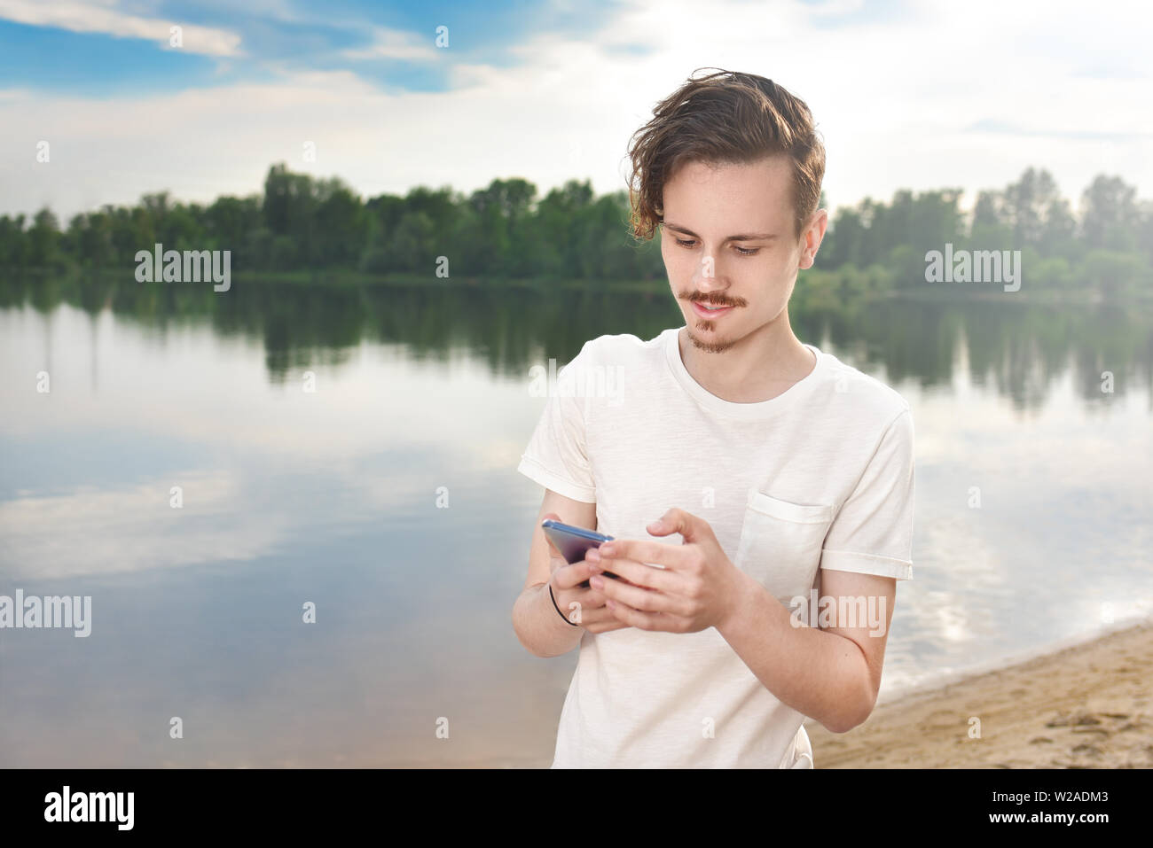 Young man walking near beautiful bay using phone and headphones for communicate with friends . good mood, beautiful view Stock Photo