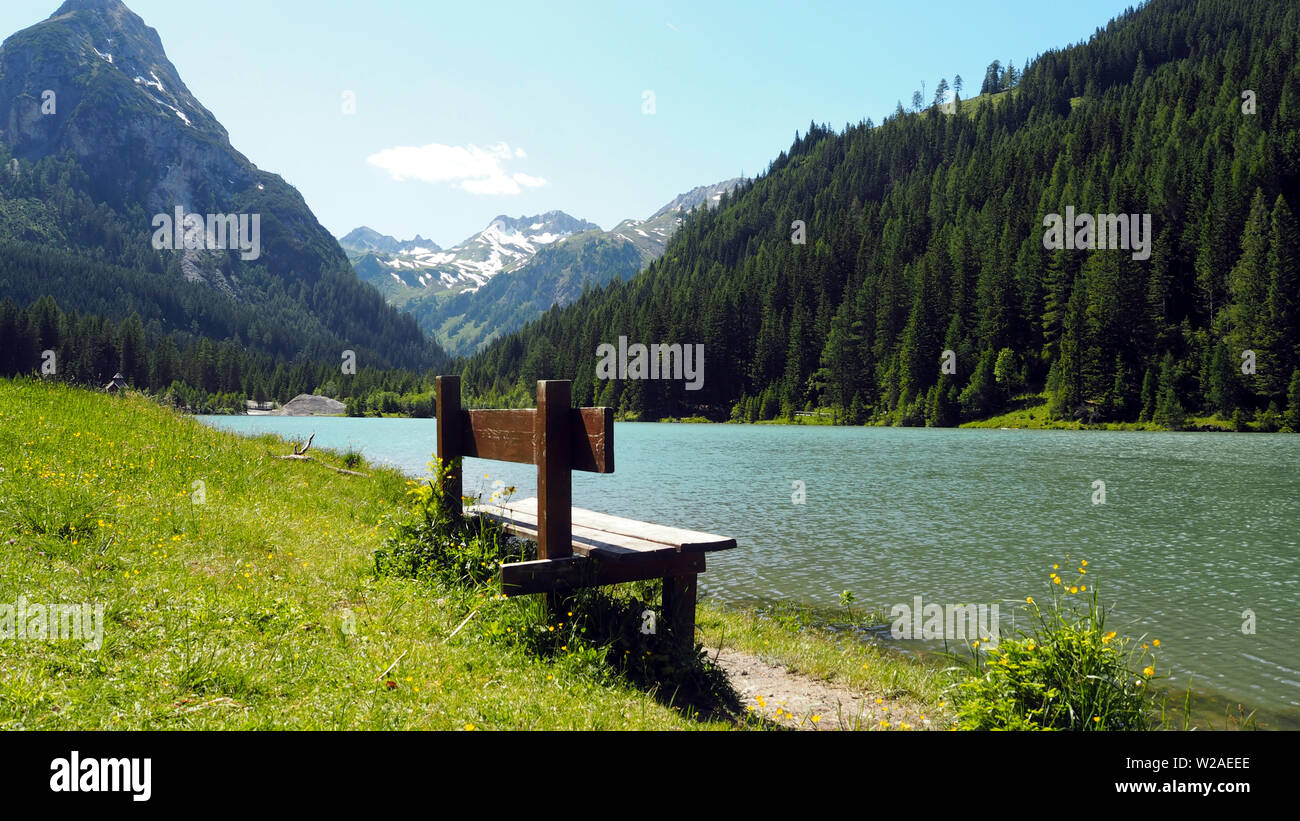 Empty Wodden Bench in front of lake Schliereralmsee with mountain scenery in Radstaedter Tauern, Niedere Tauern, Austrian Alps, Austria, June 2019 Stock Photo