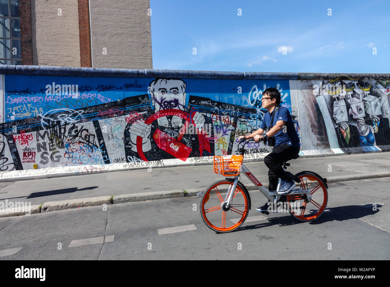 Man ride a bike Biker Mobike, East Side Wall Gallery, Berlin Wall Germany Cycling Friedrichshain city street Berlin bicycle wall Stock Photo