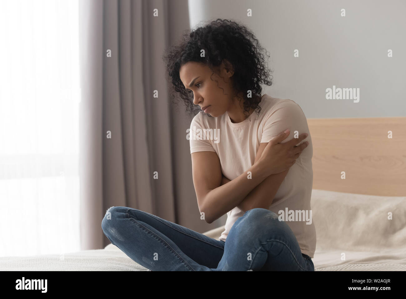 Upset depressed african woman feel sad sit alone on bed Stock Photo