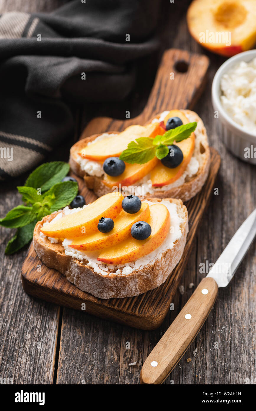 Bruschetta with ricotta cheese, peach and blueberries on wooden background Stock Photo
