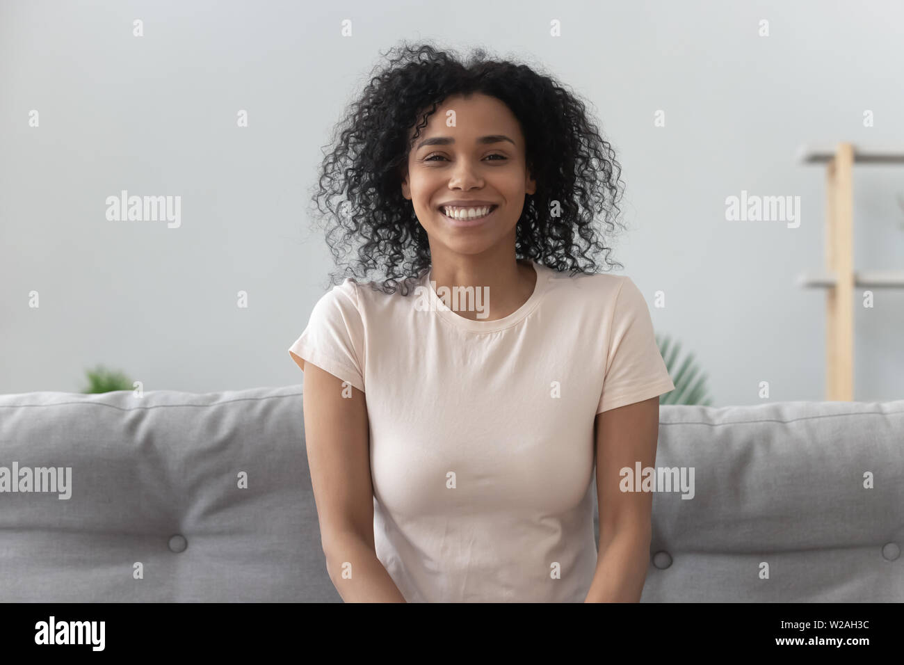 Smiling young african woman sit on sofa looking at camera Stock Photo ...