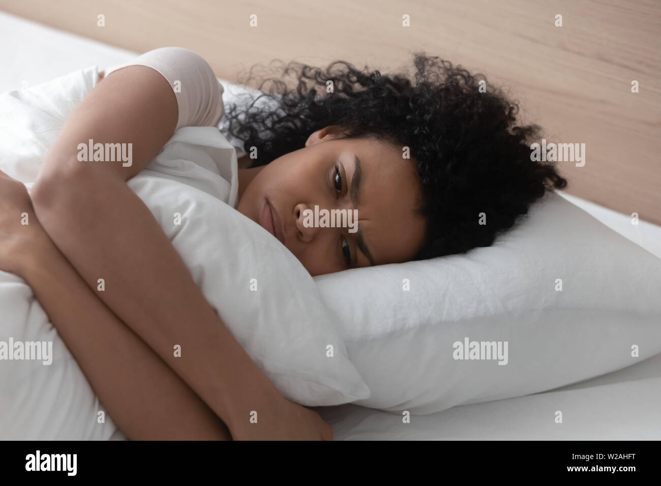 Sad depressed african woman hugging pillow lying in bed alone Stock Photo