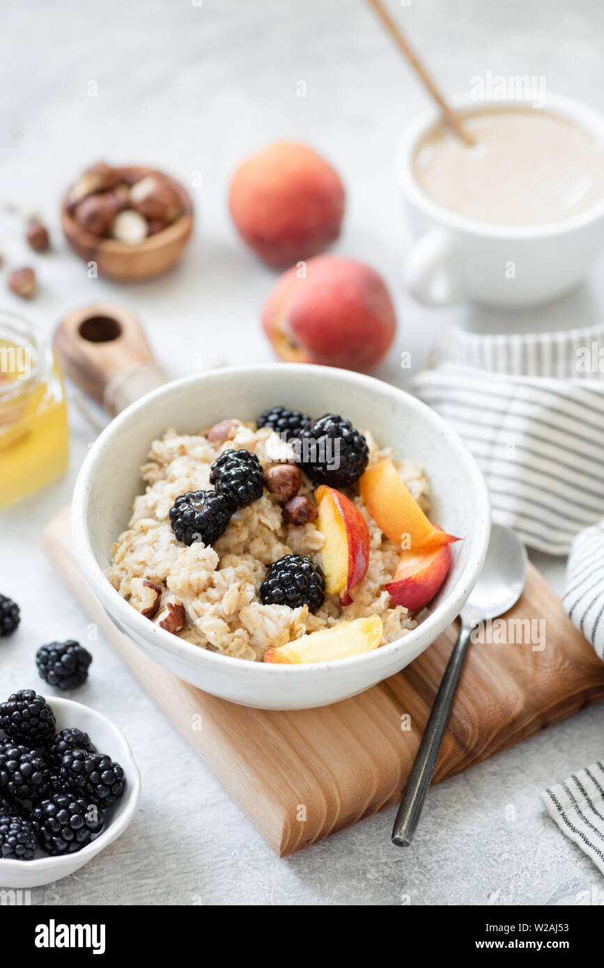 Oatmeal porridge with fruits, berries and honey in a bowl, cup of coffee with milk on background. Healthy breakfast food. Concept of clean eating, die Stock Photo