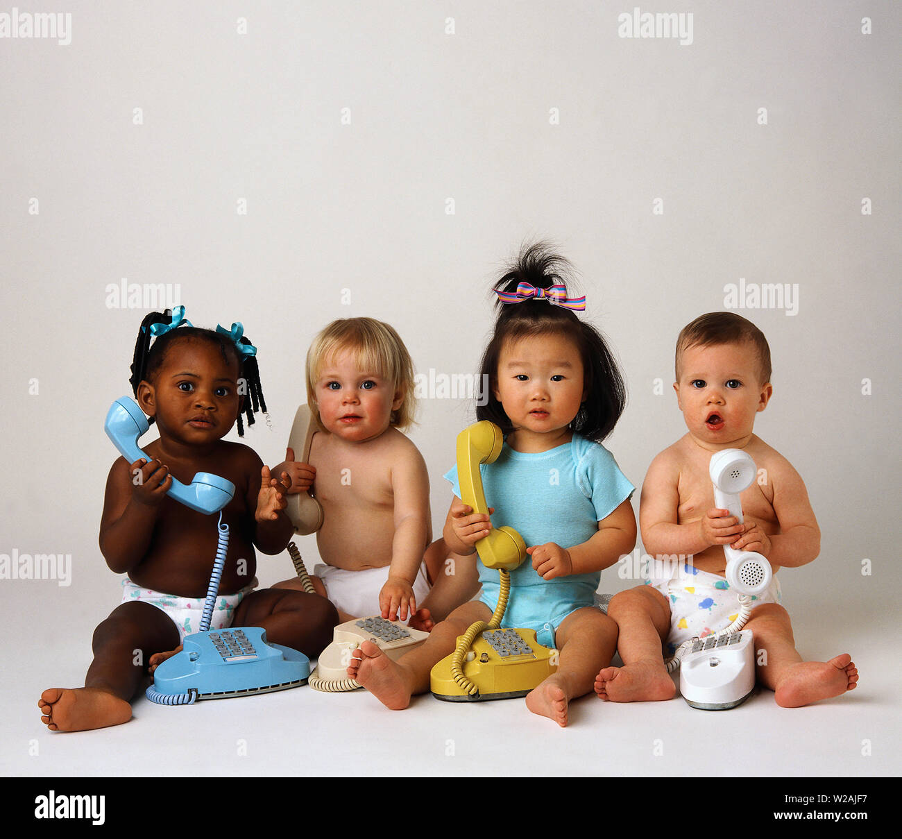 Four  babies sitting next to each other holding telephone Stock Photo