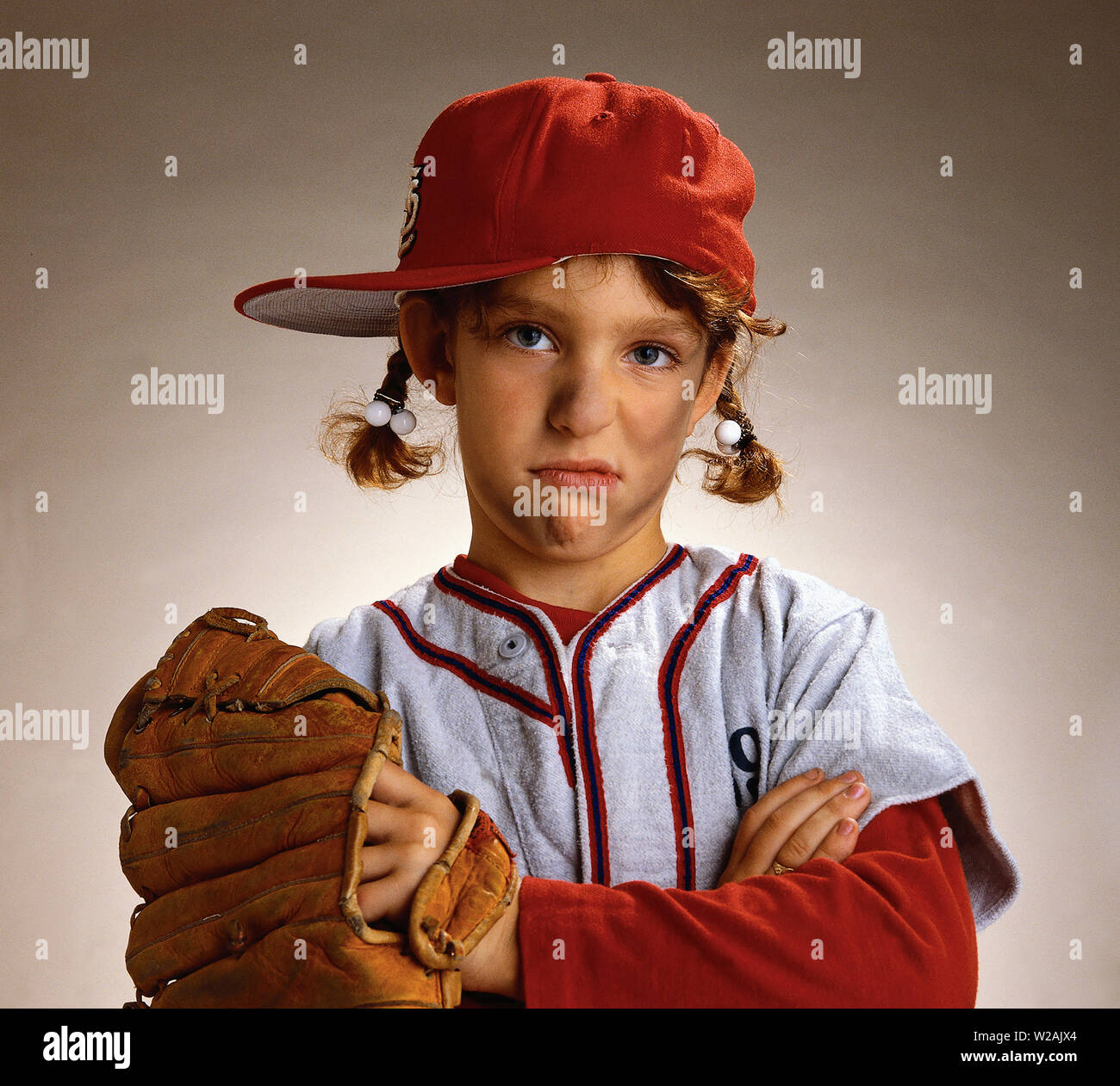 Young girl who is dressed in a baseball uniform looking very sad Stock