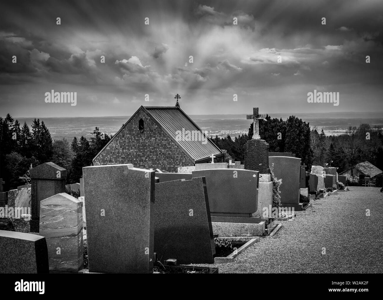 Black and white rendering of graveyards in cemetery and sun rays converging on top of a church cross - Halloween composition with space for names and Stock Photo