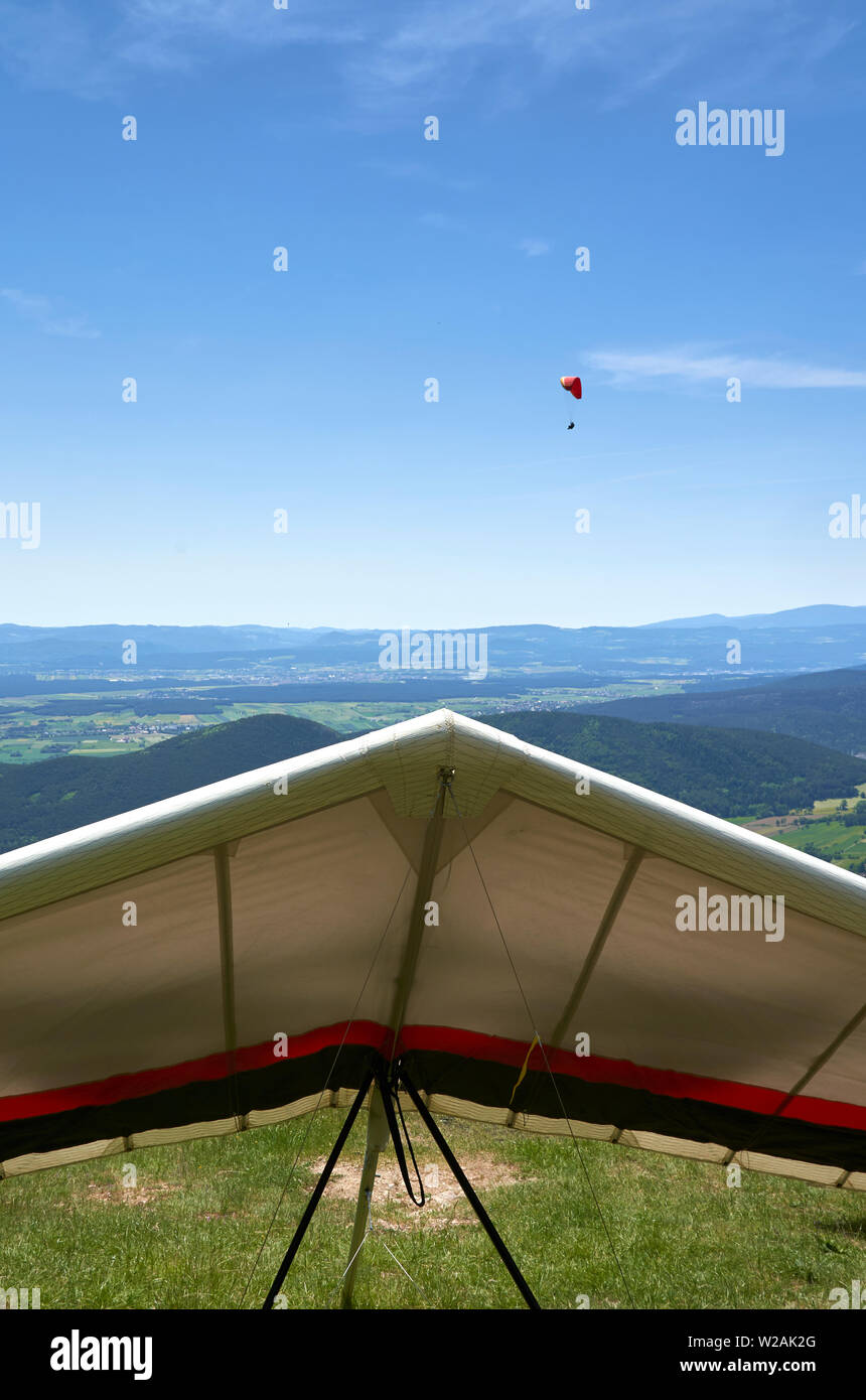 Hang glider waiting for a wind on ground and a paraglider already iin the air. Stock Photo