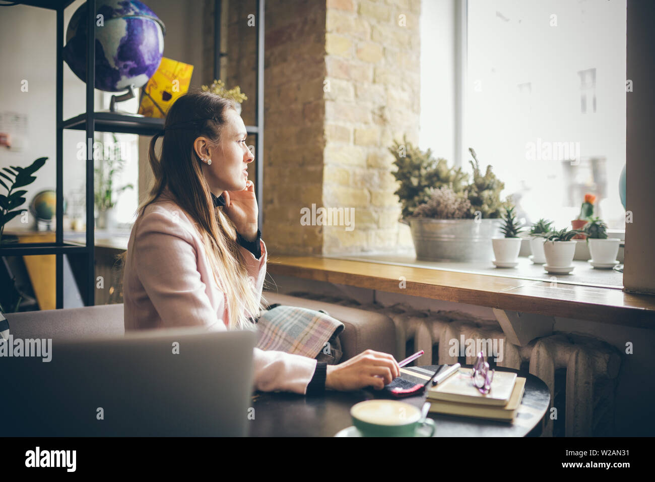 Happy Businesswoman Talking On The Phone. Woman In Cafe, use mobile Phone, Working On Notebook. Lady at cafeteria using phone and laptop, drink cup Stock Photo