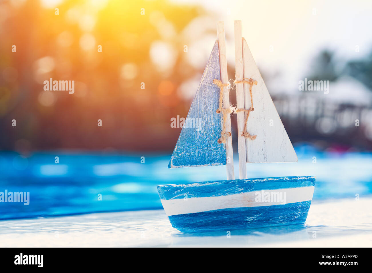 wooden toy sailboat by the swimming pool in summertime. Vacation and leisure concept concept. Stock Photo