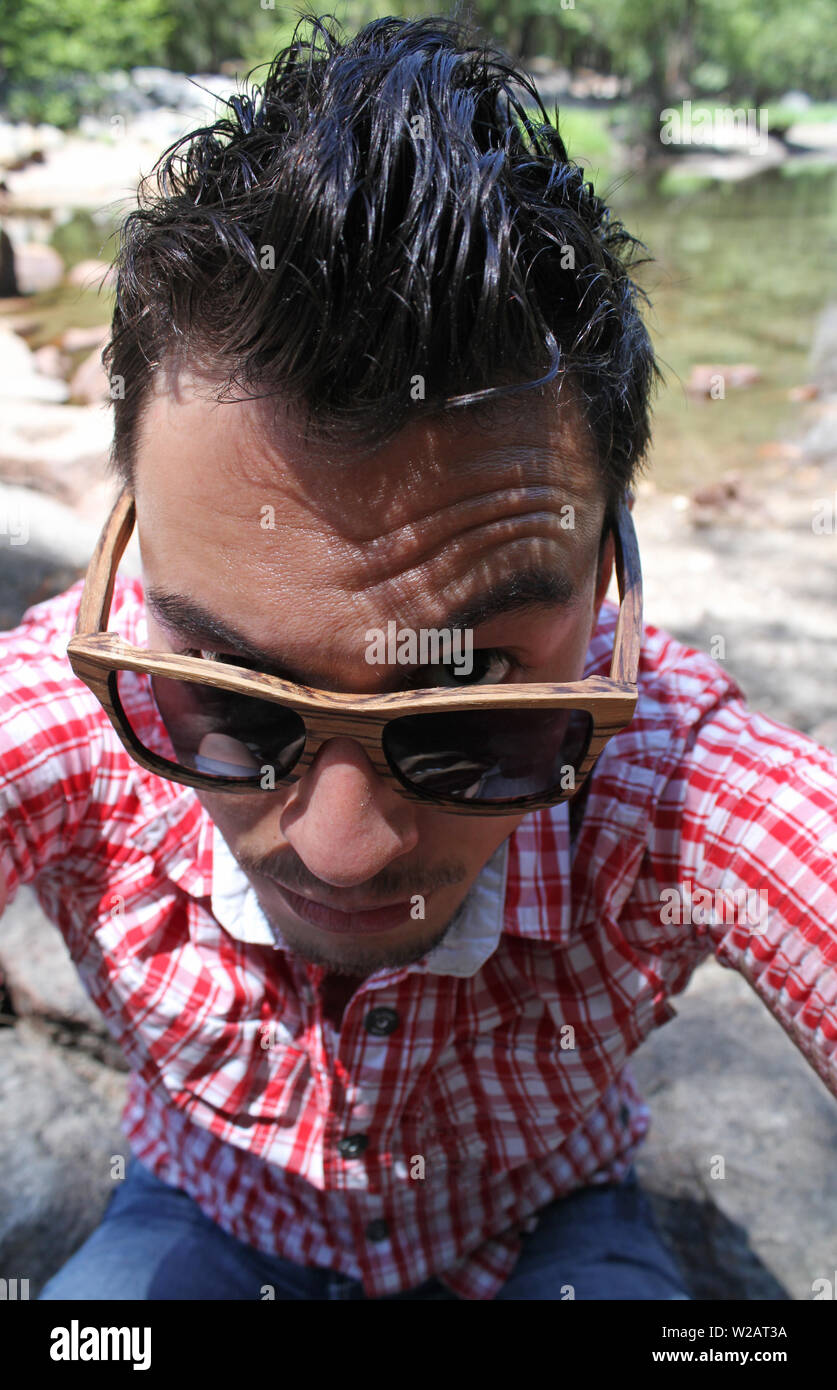 Man with dark wet hair looking over his sunglasses in a sceptical way Stock Photo