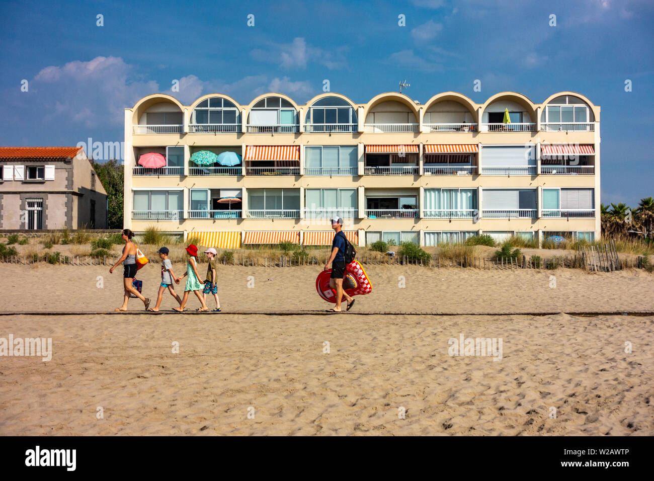 Family walking along the beach boardwalk in front of some 1980's holiday apartments Stock Photo