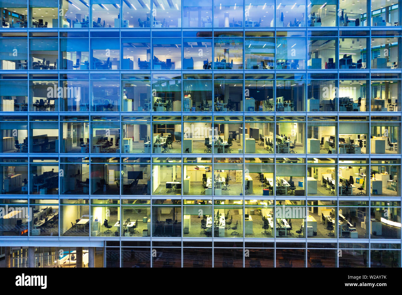 working late: looking through the glass facade at office spaces in a modern office building in the evening Stock Photo
