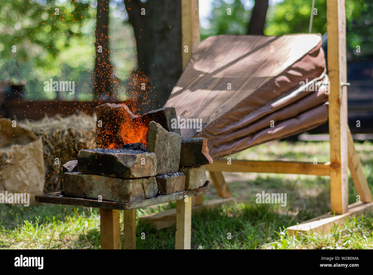 Medieval bellows make the fire of coals and sparks fly from outdoor blacksmith tool. The process of making swords and other metal tools Stock Photo