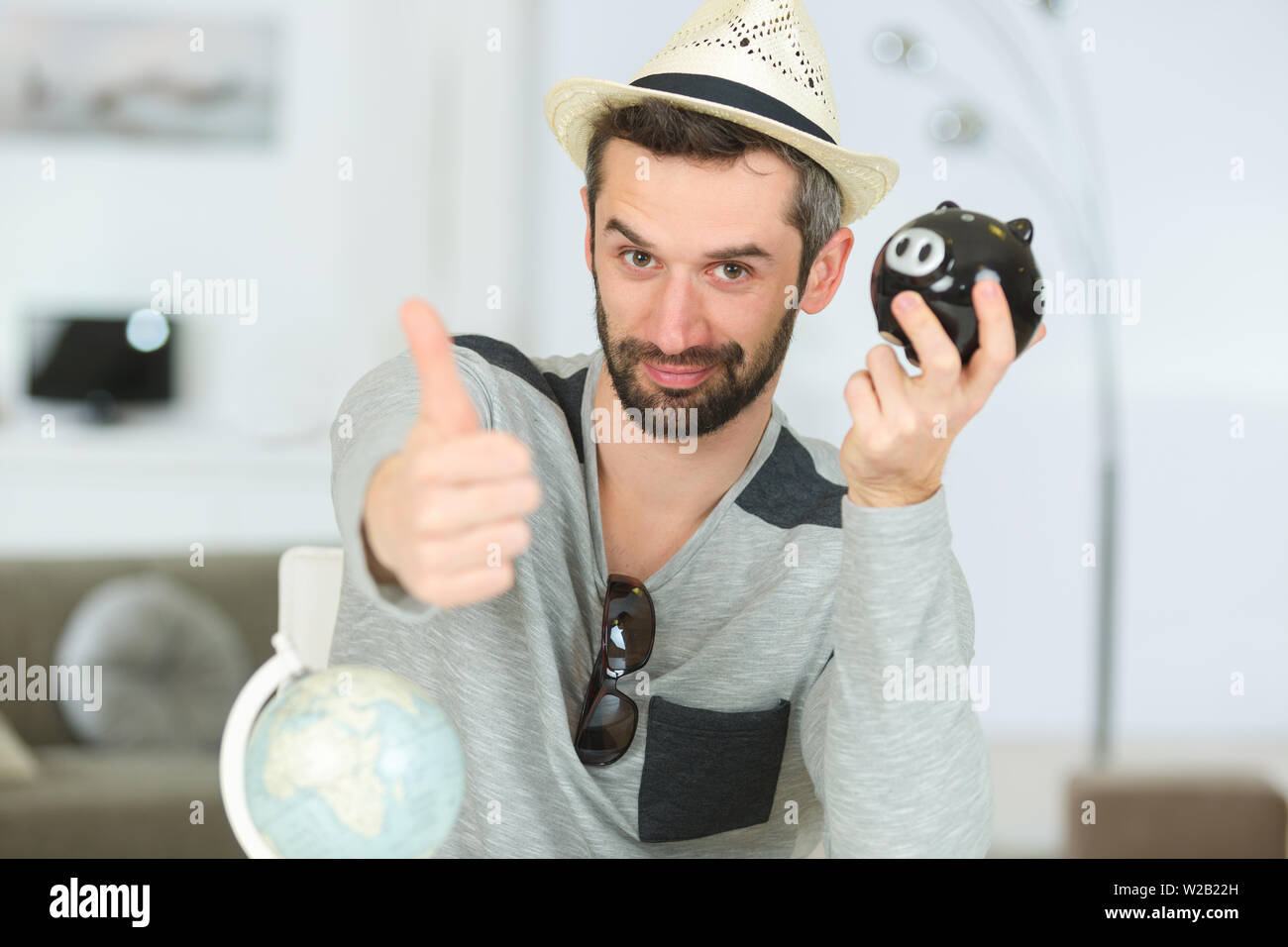 man wearing hat with globe and piggy bank Stock Photo