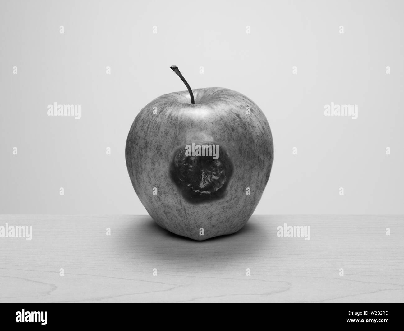 Bruised apple starting to rot on wood table. Black and white. Concept: rotten to the core, one bad apple... Stock Photo
