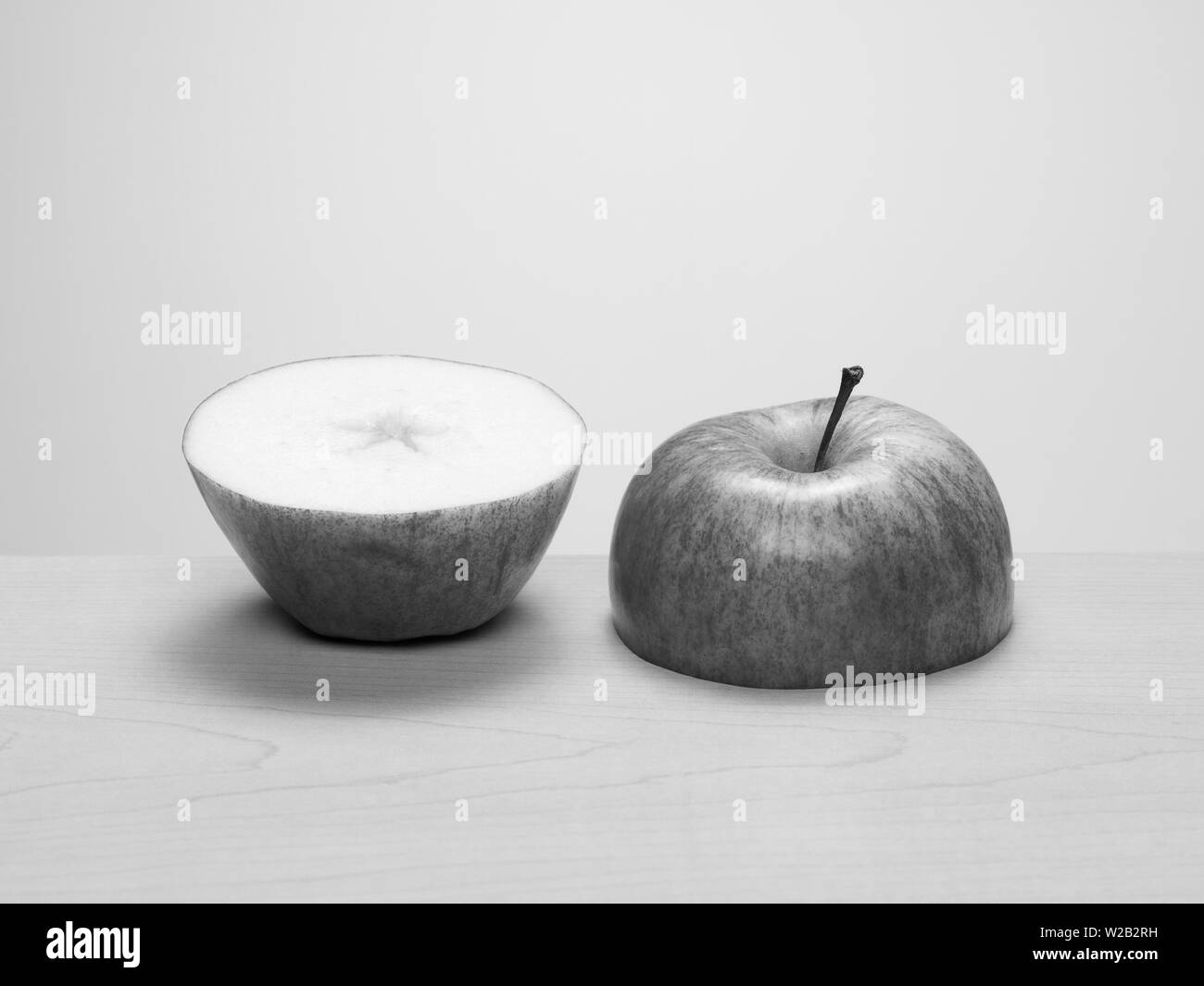 Two halves of a cut apple side by side on wood table. Black and white Stock Photo