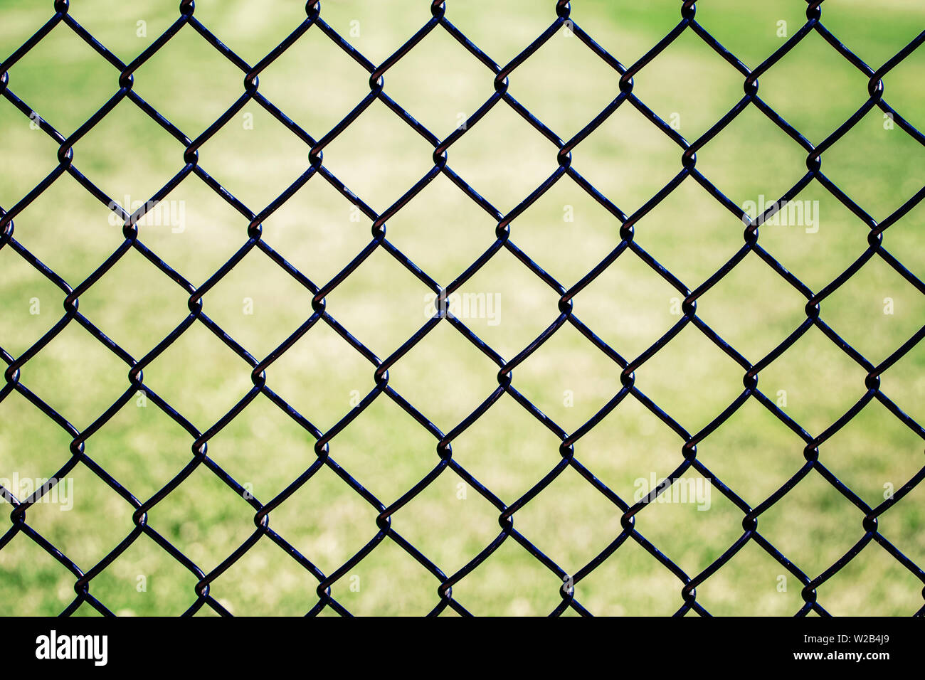 Closeup of black metal netting wire mesh fence against green field ...