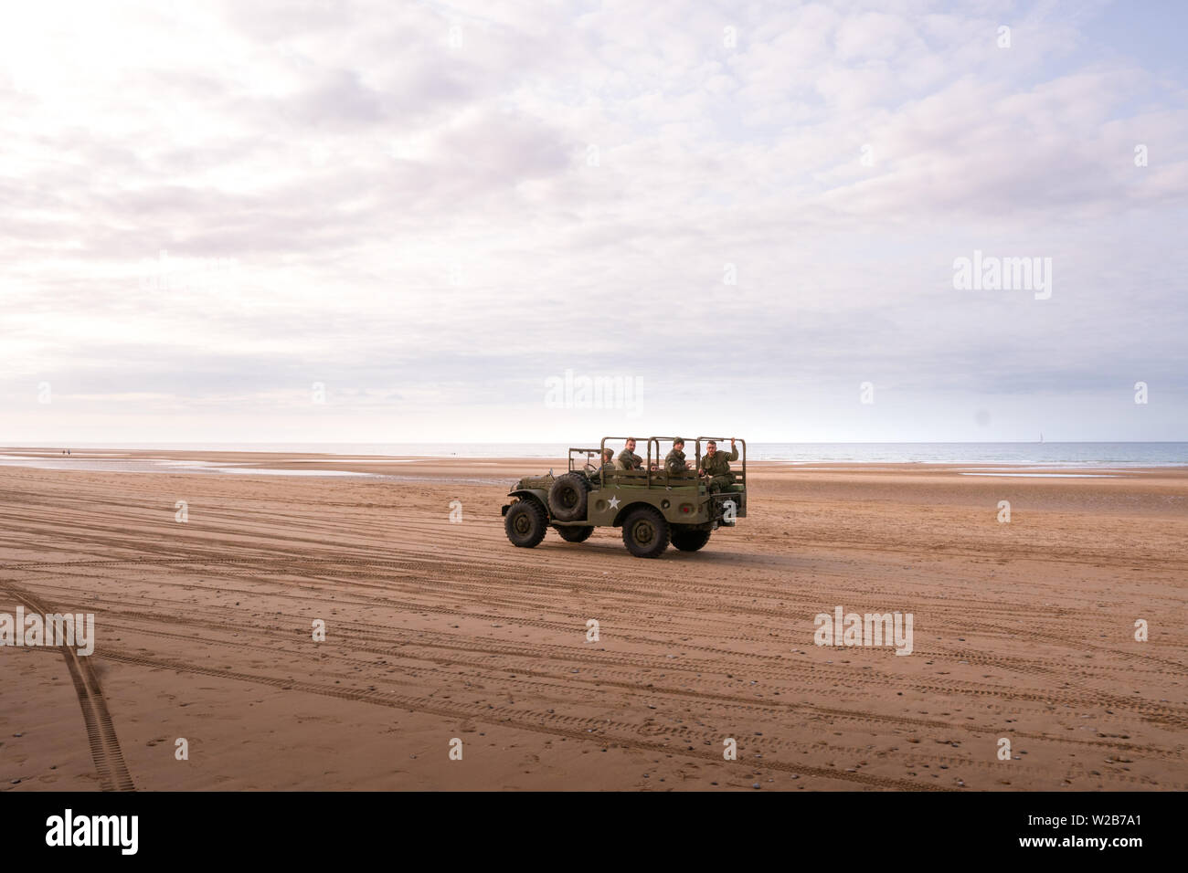 Vintage World War 2 Jeep on a beach in Normandy, driving off-road with people on board dressed in military uniforms Stock Photo