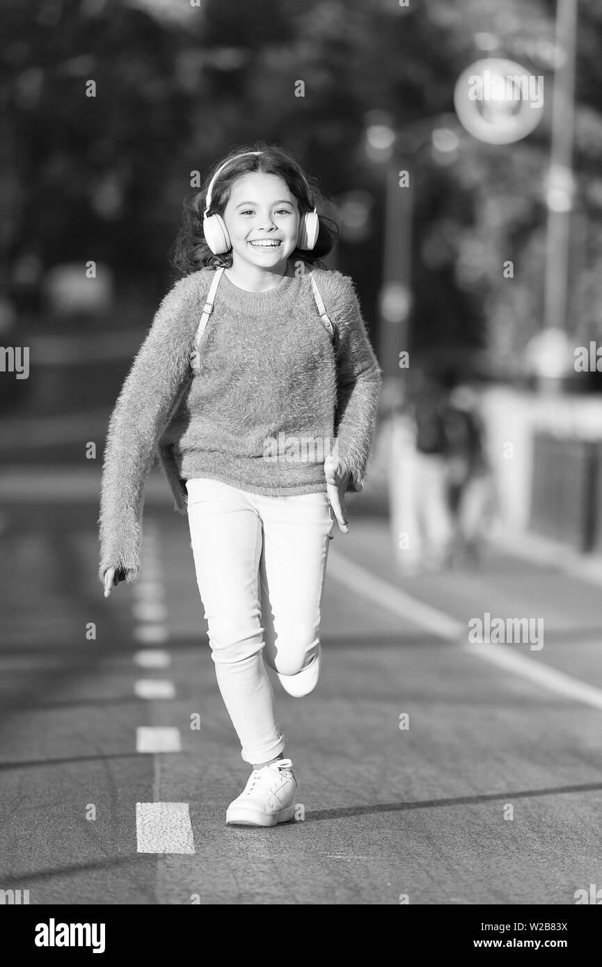 Towards happy day. Girl cute with headphones. Little child enjoy activity. Kid walking running in park listening music. Music fills me with energy. Enjoy walk with favorite music in headphones. Stock Photo