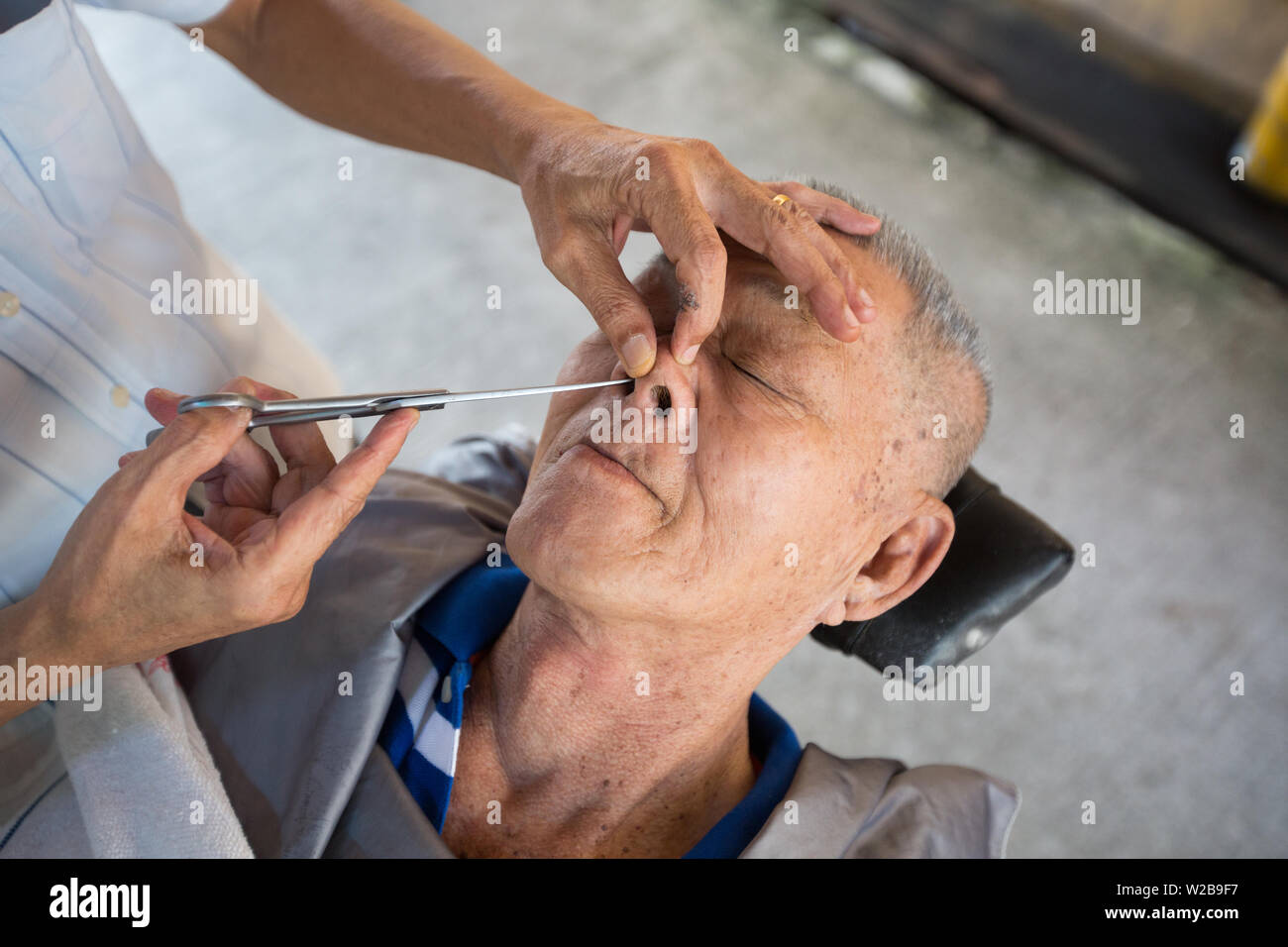 A Traditional Street Barber Using A Long Scissor To Trim An Old