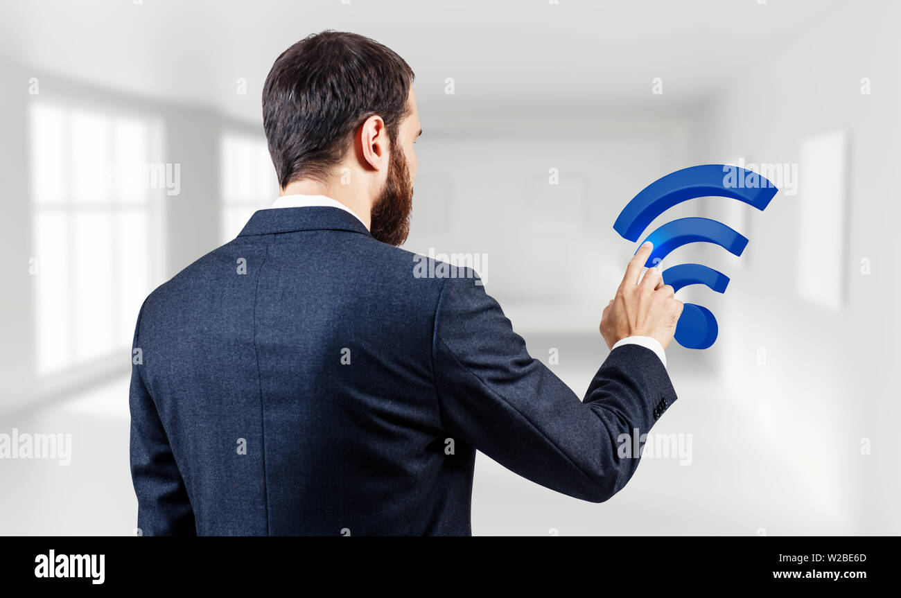 Businessman touches virtual wifi icon in the white office background. Stock Photo