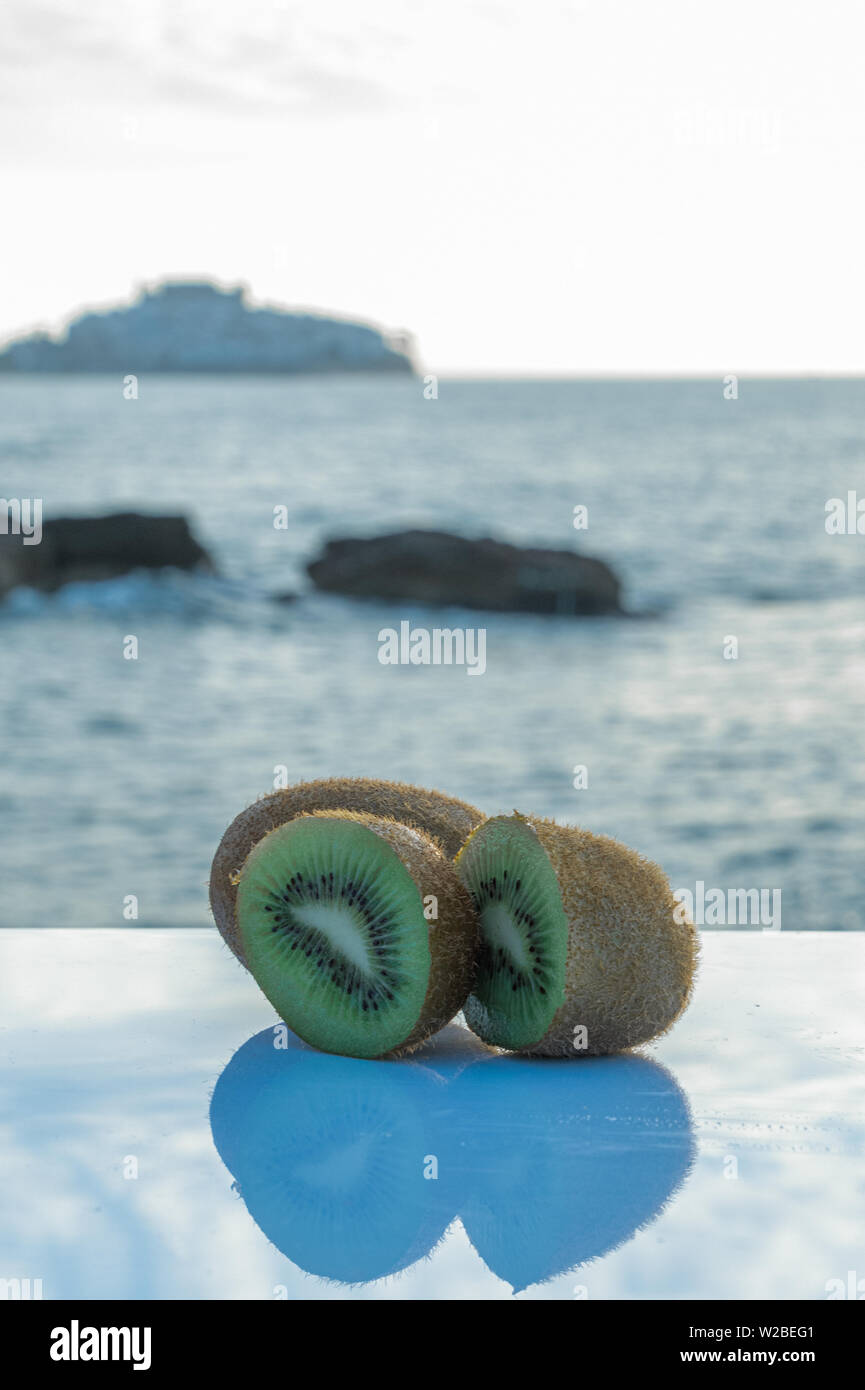 Delicious and hairy green kiwi reflecting shade on the white table - Vertical orientation - Close-up of kiwis cut in half Stock Photo