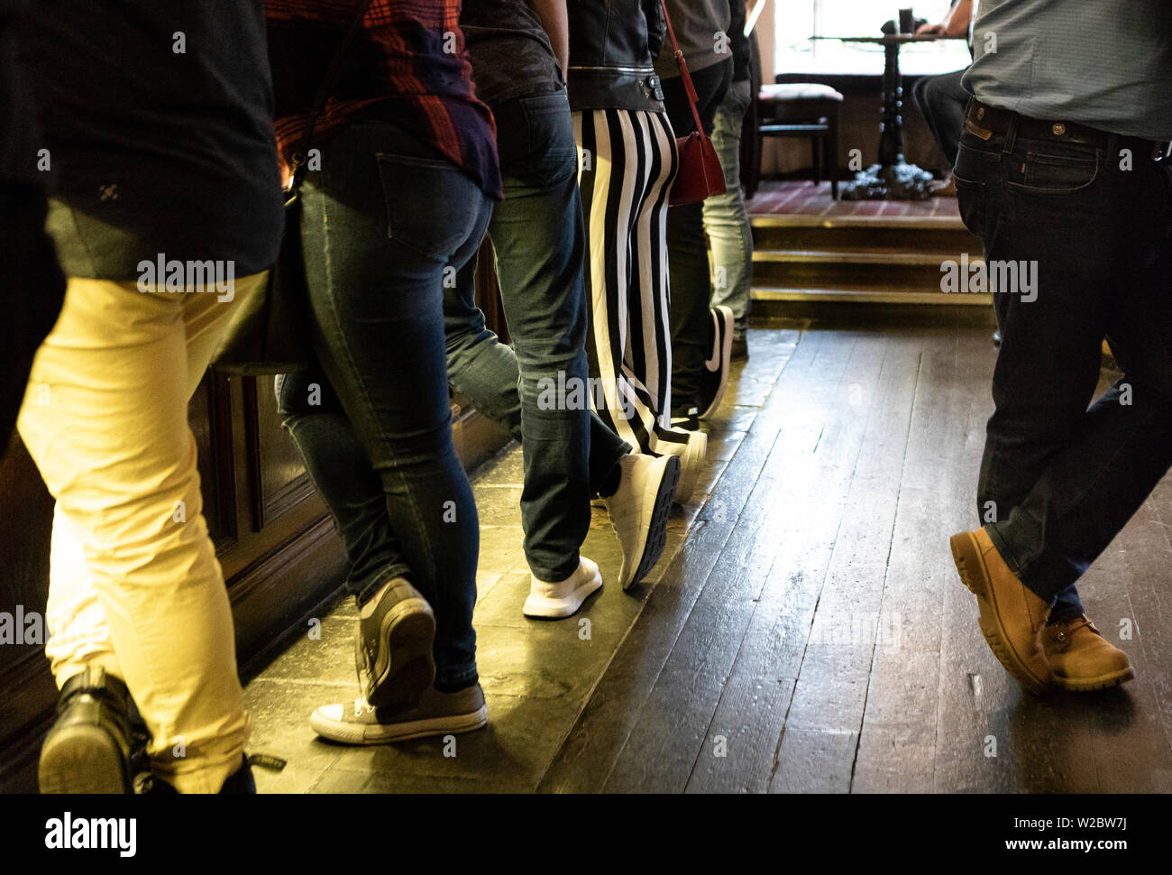 people with cropped legs stand  at a bar counter in a pup with a wooden floor Stock Photo