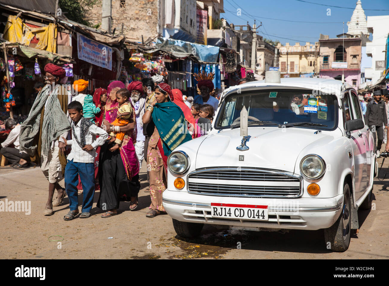 India, Rajasthan, Pushkar, People passing a white  Ambassador car on way to Pushkar camel fair Stock Photo