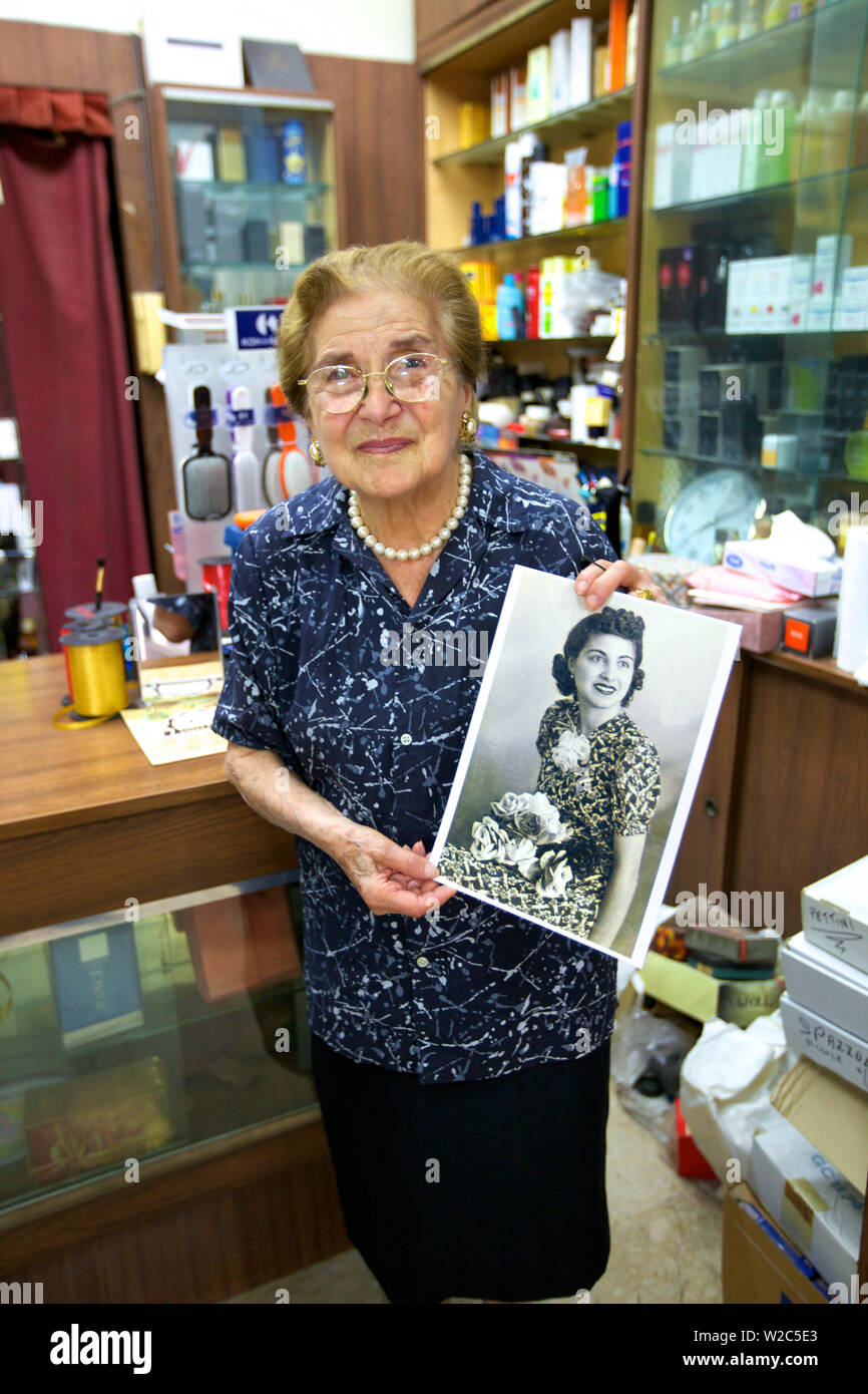 Shop Keeper Holding Old Photograph of Herself. Ortygia, Syracuse, Sicily, Italy Stock Photo