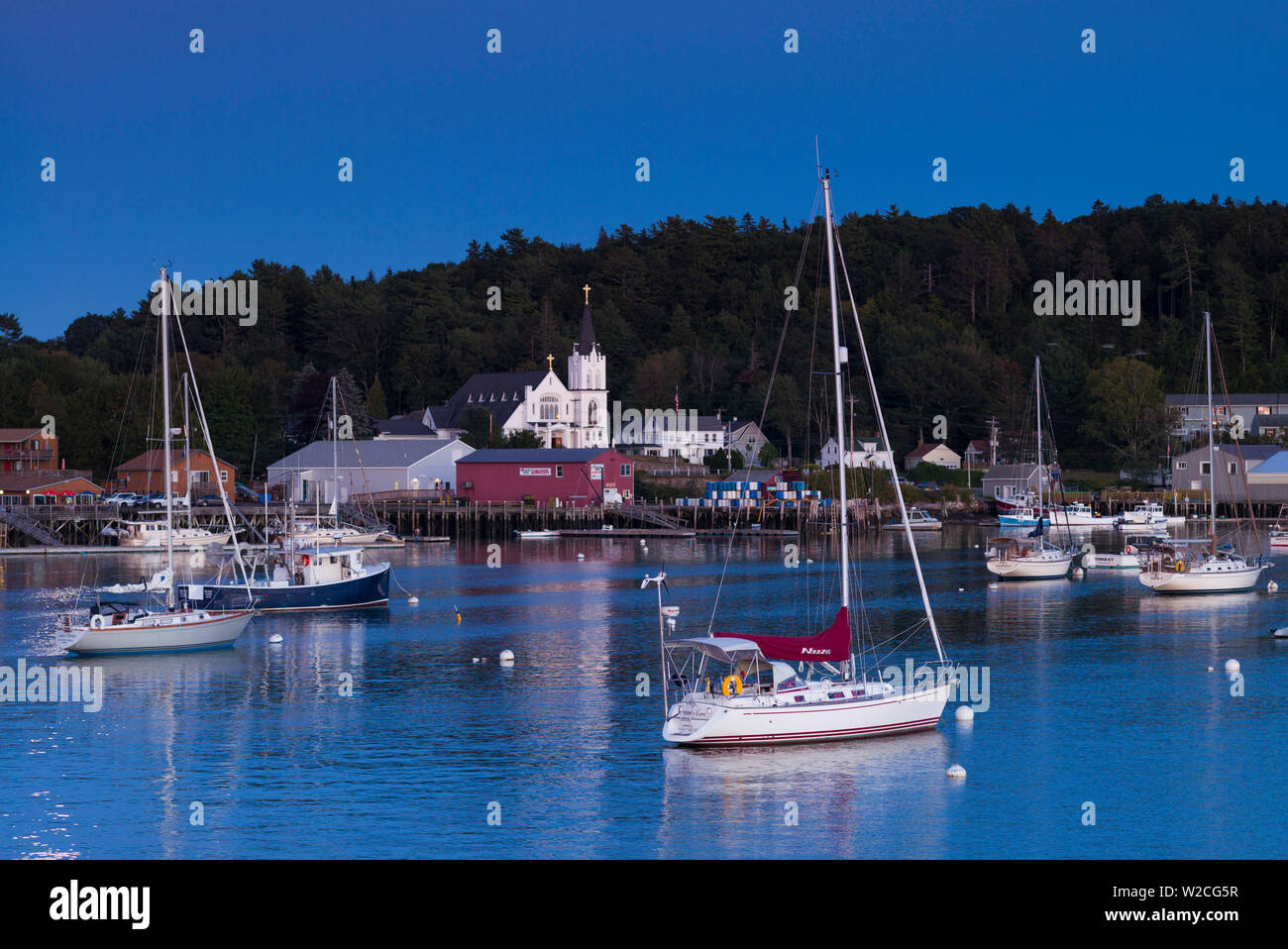 USA, Maine, Boothbay Harbor, harbor view with Our Lady Queen of Peace Catholic Church, dusk Stock Photo