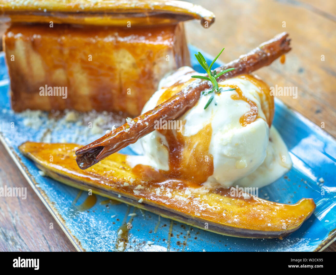 Vanilla Ice cream topping with caramel on ceramic plate on wooden table. Close-up Caramelized Banana Toast homemade dessert. Stock Photo