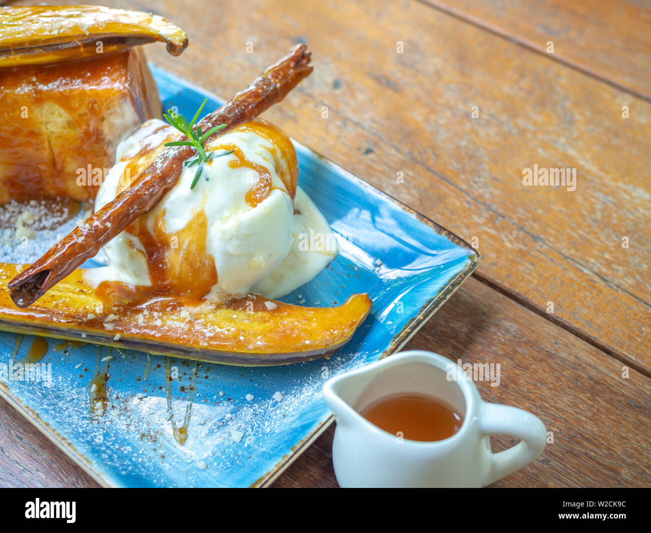 Vanilla Ice cream topping with caramel on ceramic plate on wooden table with copy space. Close-up Caramelized Banana Toast homemade dessert. Stock Photo