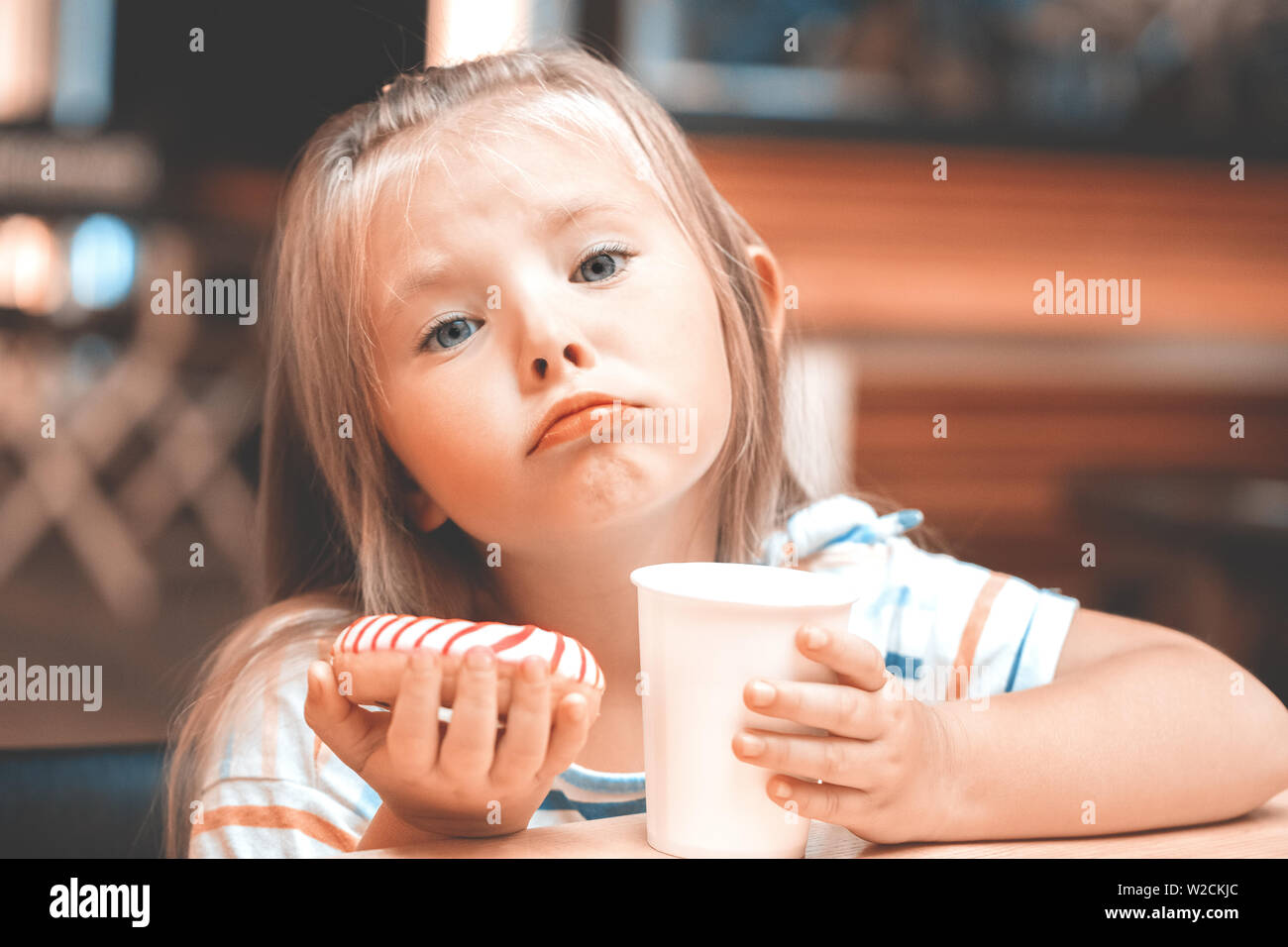 Cute little girl eat stripsed donut on cafe shop. This image has a vintage, film grain look. Stock Photo
