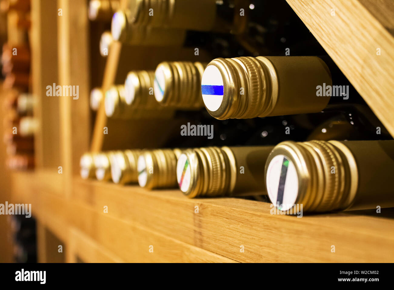 Bottles of white wine with golden colored wrap laying down on the wooden shelf in dark,fresh cellar Stock Photo