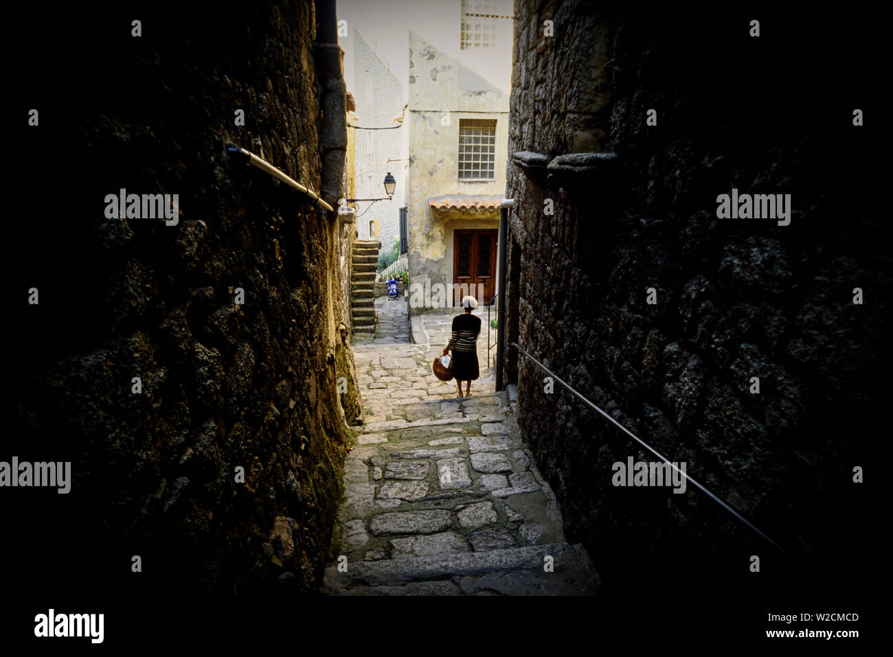 Sartene, Corsica, France. A woman walks down an alleyway. Photo: © Simon Grosset. Archive: Image digitised from an original transparency. Stock Photo
