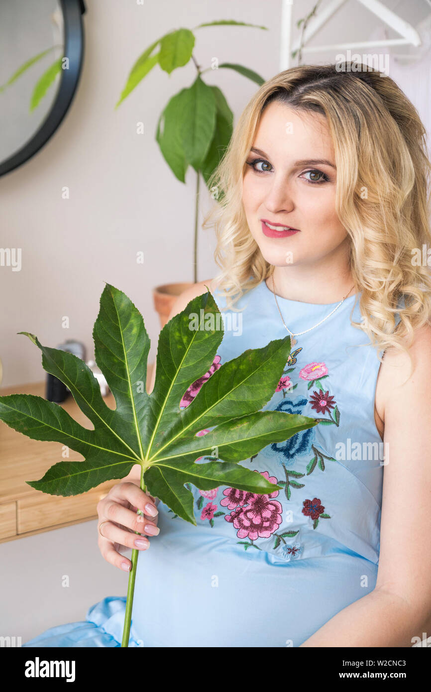 photo of pregnant blonde girl holding a plant with large green leaves Stock Photo
