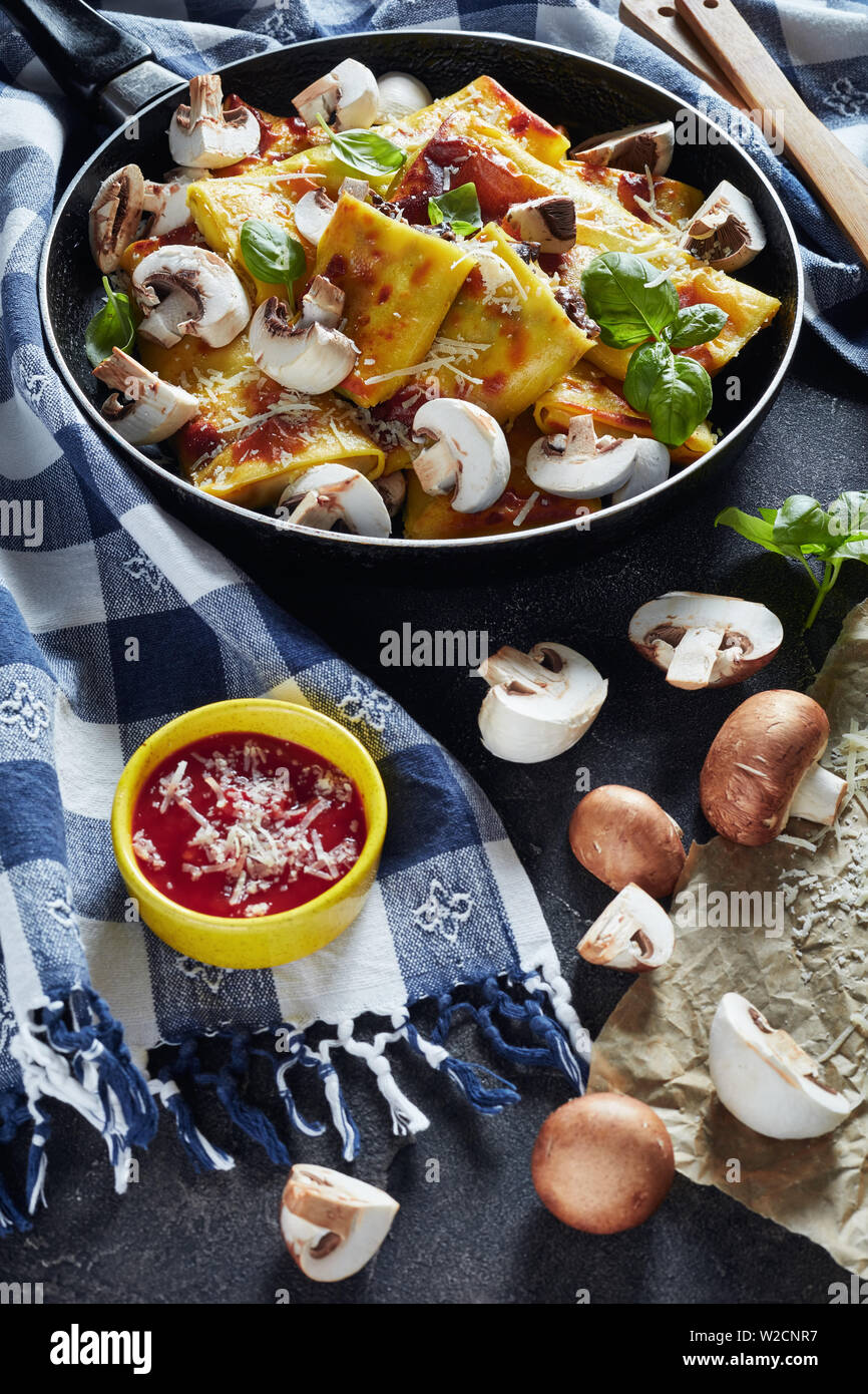 delicious Crepes with parmesan and mushrooms filling on a skillet on a concrete table with tomato sauce and kitchen towel, vertical view Stock Photo